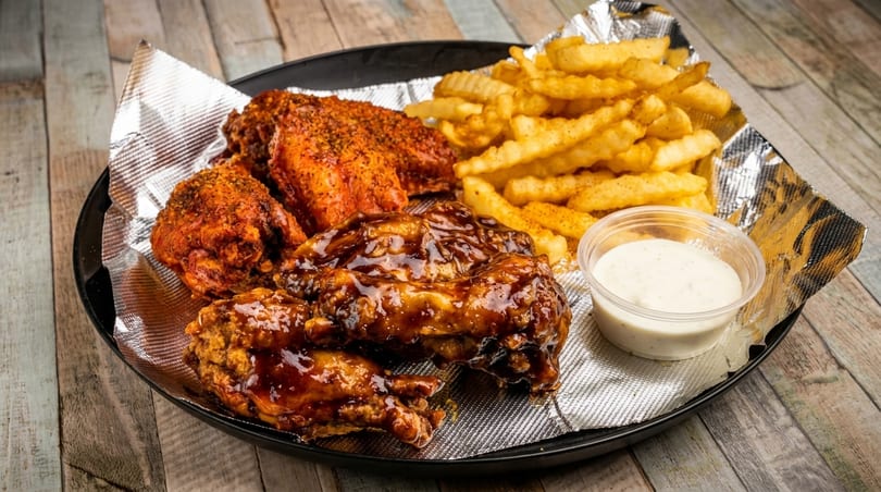 A platter of crispy chicken wings, some sauced and some dry-rubbed, with crinkle-cut fries and ranch.