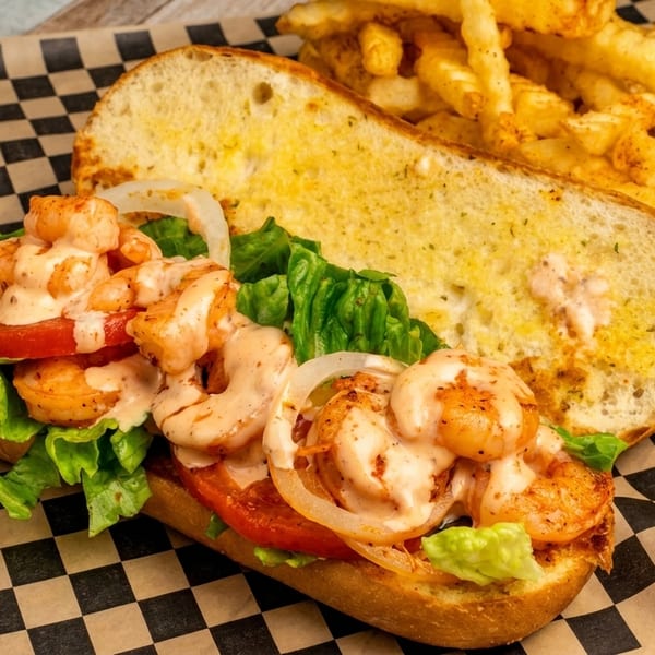 Shrimp po'boy sandwich with lettuce, tomato, onion, and sauce, served with french fries.