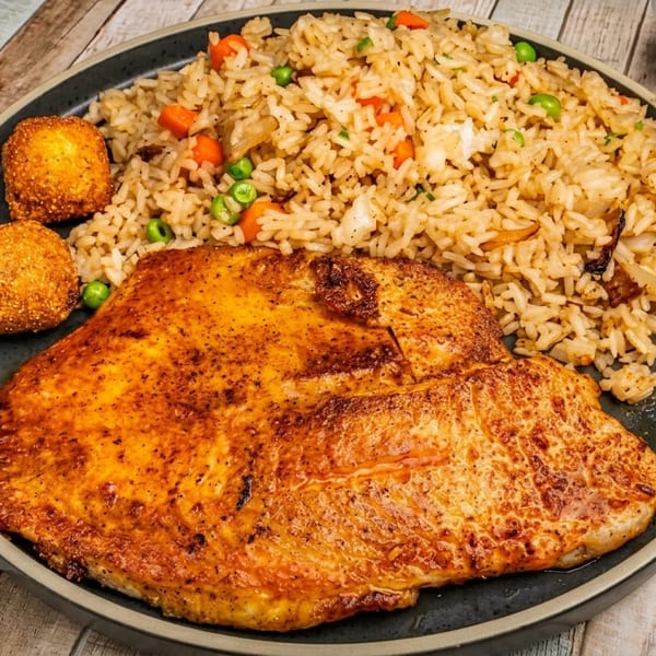 A plate of fried rice with peas and carrots, a large piece of grilled fish, and two fried balls.