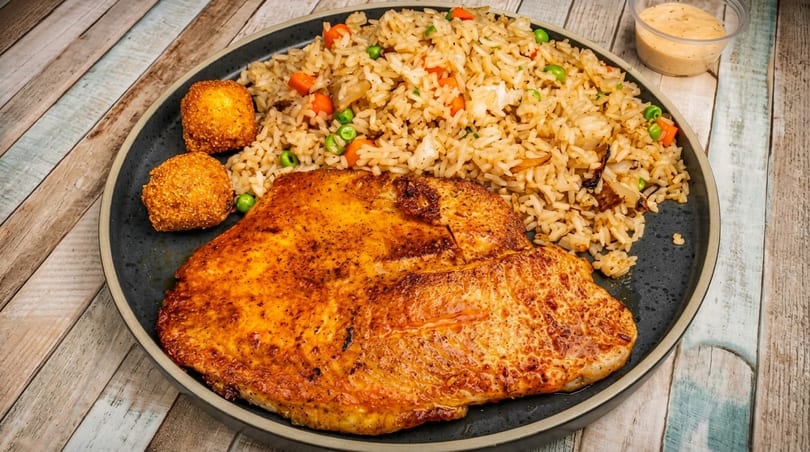 A plate of fried rice with peas and carrots, a large piece of grilled fish, and two fried balls.