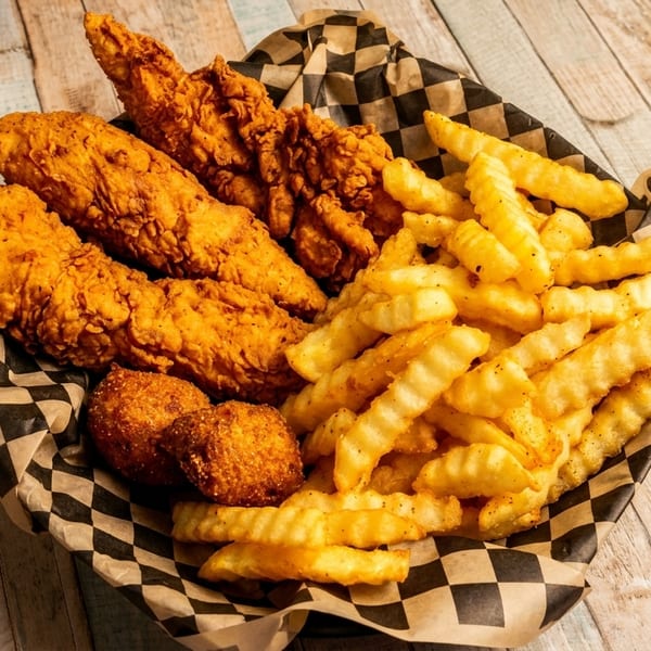 A basket of crispy fried chicken tenders, hush puppies, and crinkle-cut fries with dipping sauce.
